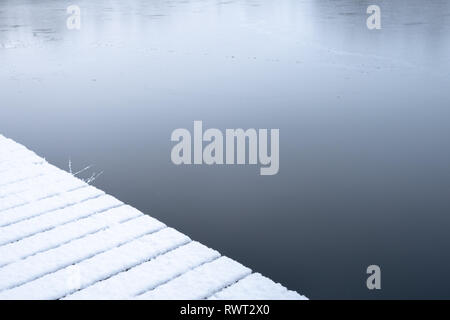 Una coperta di neve jetty accanto al lago di criminalità in un freddo inverno mattina Foto Stock