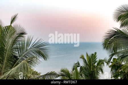 Bellissimo paesaggio da un isola costiera con palme, calmo mare Arabico e l'orizzonte chiaro, durante il tramonto con magica luce del sole caldo colore Foto Stock