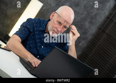 Un imprenditore senior utilizzando laptop, egli sta avendo difficoltà e problemi di visione Foto Stock