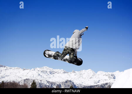 Extreme Jumping Snowboarder a saltare sopra le montagne in giornata di sole Foto Stock