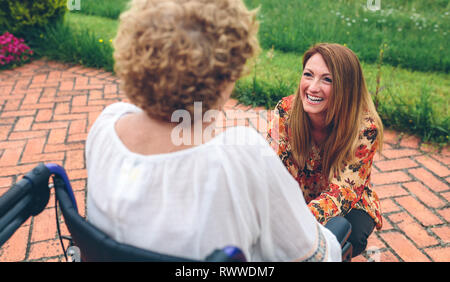 Giovane donna cura donna anziana in una sedia a rotelle Foto Stock