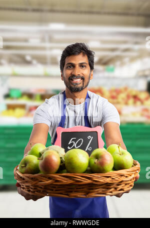 Indian negozio o supermercato dipendente maschio sorridente come offerta di mele a metà prezzo dal carrello Foto Stock