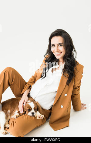 Bella donna incinta in tuta marrone stroking cane su sfondo bianco Foto Stock