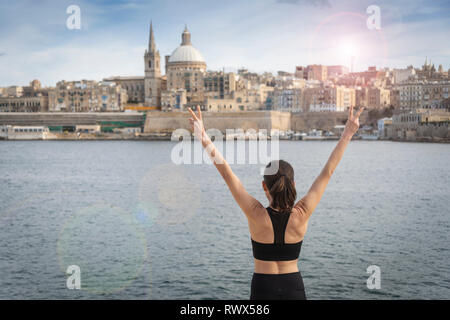 Donna in piedi di fronte a La Valletta, Malta, con le braccia aperte, libertà di viaggio. Foto Stock
