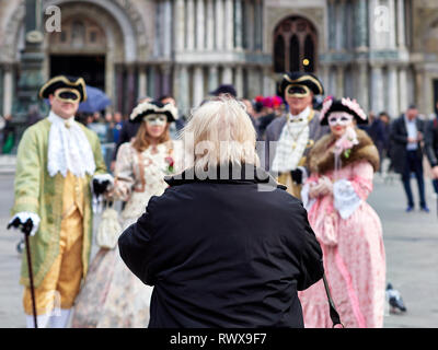 Venezia, Italia - Marzo 1, 2019 Un turista preparare per scattare una foto di un gruppo di persone mascherati nel carnevale di Venezia in Piazza San Marco durante t Foto Stock