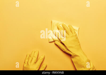 Un mani in una gomma di guanto protettivo con una spugna bianca su sfondo giallo. Il concetto di pulizia. Foto Stock