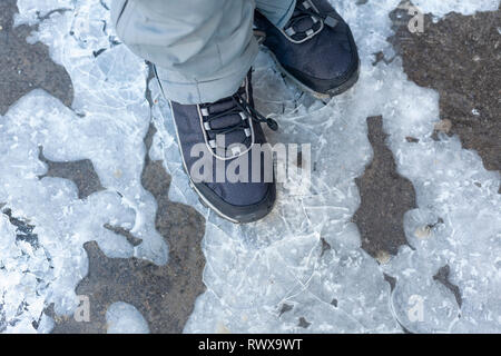 Bambino passi sulla pozza congelati con ghiaccio sottile. Close up. Foto Stock