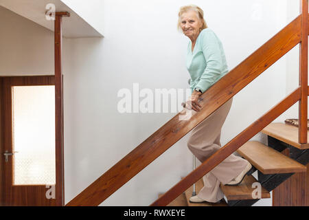 Donna anziana a casa usando un bastone da passeggio per scendere le scale Foto Stock