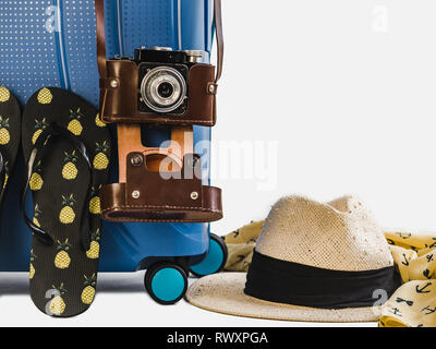 Elegante, blu valigia, Elegante cappello per il sole e le scarpe da spiaggia. Bianco, isolato sfondo. Close-up. Vista laterale. Preparazione per il viaggio estivo Foto Stock