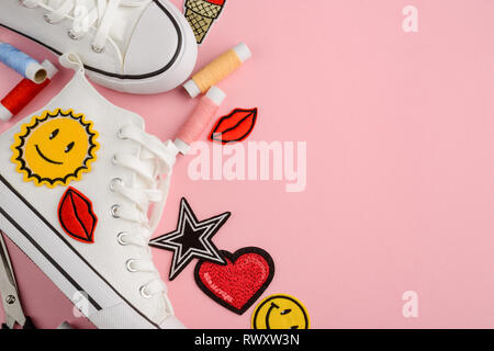 Design personalizzato per il bianco sneakers. Scarpe nuove, diverse cool patch e filettature su sfondo rosa. Foto Stock