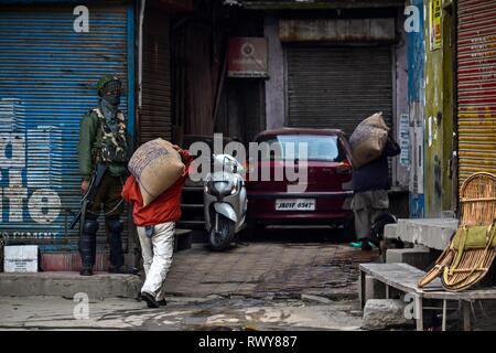 8 marzo 2019 - Srinagar, J&K, India - lavoratori visto il trasporto del carico in quanto a piedi passato un soldato di paramilitari durante le restrizioni a Srinagar, Kashmir indiano. Le autorità impongono delle restrizioni in parti della città in vista di un strike chiamato dai separatisti contro slapping della pubblica sicurezza atto (PSA) sul presidente JKLF Yasin Malik e divieto di Jaamat-e-Islami Credito: Saqib Majeed SOPA/images/ZUMA filo/Alamy Live News Foto Stock