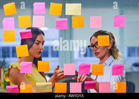 Due caucasian donne mature discutere le idee su adesivi in ufficio. Vista attraverso la finestra Foto Stock