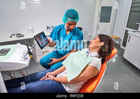 Maschio africano dentista spiegando raggi x al paziente seduto in poltrona Foto Stock