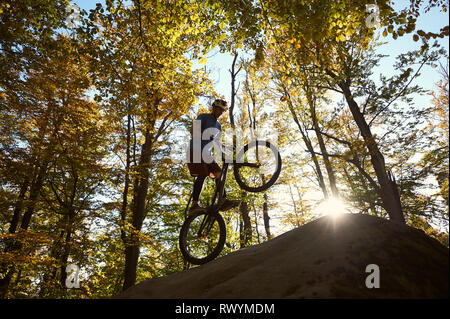 Silhouette di un ciclista professionista in piedi sulla ruota posteriore in prova bicicletta, sportivo di bilanciamento del pilota sul bordo del grosso masso nella foresta. Concetto di sport estremo che uno stile di vita attivo Foto Stock