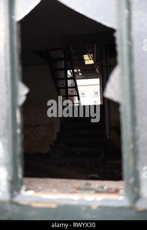 Il peering attraverso un vetro rotto in un edificio abbandonato. Foto Stock