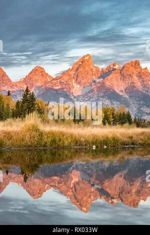 Montagne brillare rosso di sunrise, Grand Teton Range gamma di montagna si riflette nel fiume, paesaggio autunnale su Snake River Foto Stock