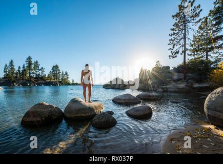 Giovane donna in bikini in piedi su una pietra rotonda in acqua, baia presso il lago di Lake Tahoe, Sand Harbor State Park, shore, California Foto Stock