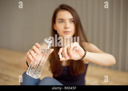 Close-up di una ragazza è in possesso di una pillola sport con additivi per la formazione e una bottiglia di acqua. Foto Stock