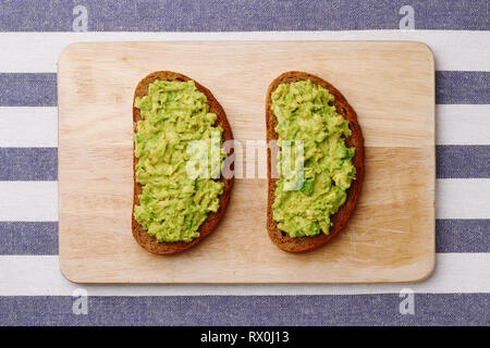 Sandwich con il guacamole su luce sfondo tessili vista dall'alto. panini sulla tavola di legno Foto Stock