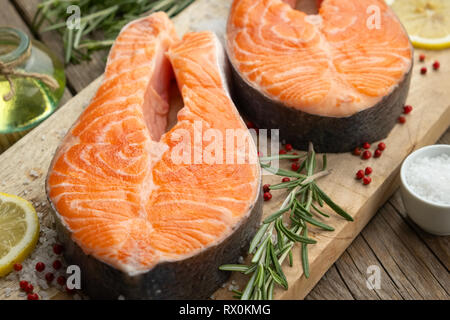 Due materie di salmone tranci di pesce con fette di limone, il sale e il rosmarino sul bordo di taglio. Foto Stock