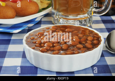 Una scodella di fagioli cotti su un tavolo da picnic con la birra e i cani di mais Foto Stock