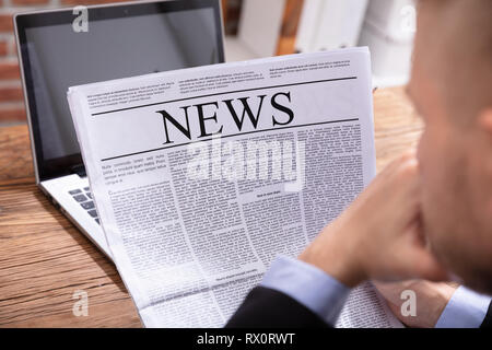 Close-up di una mano di un uomo azienda giornale sulla scrivania in legno Foto Stock