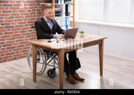 Imprenditore disabili seduti sulla sedia utilizzando laptop al lavoro Foto Stock