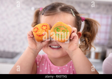 Ragazza sorridente avendo divertimento tenendo i tortini in mani che coprono gli occhi Foto Stock