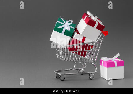 Mini carrello piena di colorati confezioni regalo con nastri. Sfondo grigio con copia spazio. Foto Stock