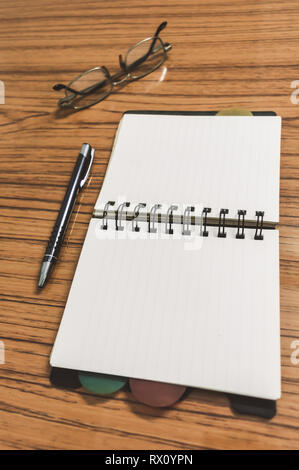 Scrivania con il notebook aperto con pagine vuote, occhiali e una penna. Business ancora il concetto di vita con office roba sulla tabella. Istruzione, lavoro e planni Foto Stock