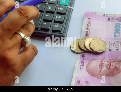 Donna controllo conto con la calcolatrice e tenendo una penna con la valuta indiana constata monete. Arrotino donna o ispettore finanziario rendendo relazione, calc Foto Stock