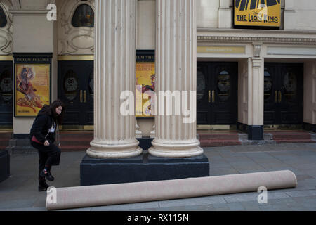 Una giovane donna passi oltre un arrotolamento a tappeto prima di srotolare montatori e tagliarlo per l interno del Lyceum Theatre sul Wellington Street, il 5 marzo 2019, a Londra, in Inghilterra. Foto Stock