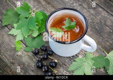 Smaltato tazza di tè di frutta con ribes nero bacche sul tavolo in legno all'esterno. Vista dall'alto. Foto Stock