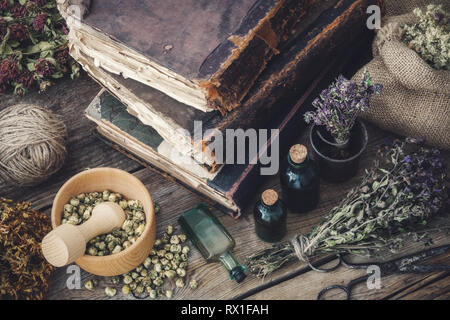Tintura di bottiglie, assortimento di secca erbe sane, vecchi libri, Malta, forbici su una vecchia scrivania in legno. La medicina di erbe. Vista dall'alto. Foto Stock