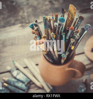 Pennelli in una brocca da potters argilla, palette di legno e tubi di vernice. Foto Stock