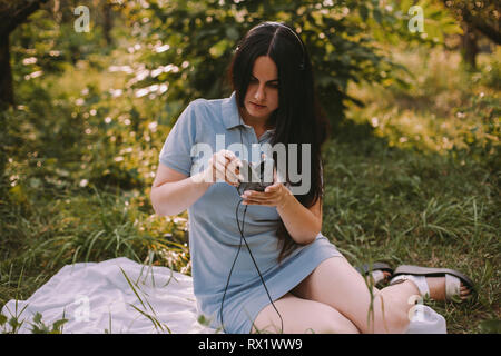 Donna con capelli lunghi ascoltare musica mentre è seduto sul campo erboso in giardino Foto Stock