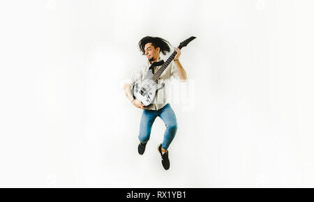 Il chitarrista divertente con gesto tenendo la sua chitarra elettrica durante il salto, isolato su sfondo bianco Foto Stock
