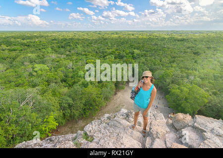 Angolo alto ritratto di donna che indossa gli occhiali da sole e cappello mentre si sta in piedi sul monte contro il verde paesaggio Foto Stock