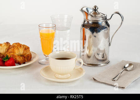 Color crema e piastra di tazza di caffè con due cornetti e tre fragole fresche su un lino bianco tovaglia e un Silver Hotel Servizio in camera caraffa Foto Stock