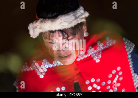 La luce soffusa illumina il volto dipinto di una donna delle prime nazioni e dei suoi regalia cerimoniali, Comox, Comox Valley, Vancouver Island, British Columbia, Canada Foto Stock