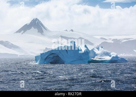 Un pinnacolo roccioso si erge alto dietro un iceberg che galleggia nello stretto di Bransfield all'interno della penisola antartica, dello stretto di Bransfield, della penisola antartica e dell'Antartide Foto Stock