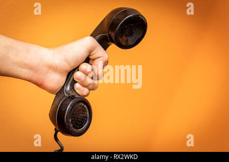 Mano che tiene il vecchio ricevitore telefonico su sfondo arancione. Foto Stock