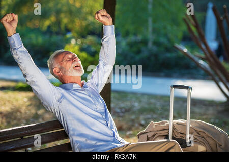 Senior gentleman seduto su una panca in legno e rilassante in un parco Foto Stock