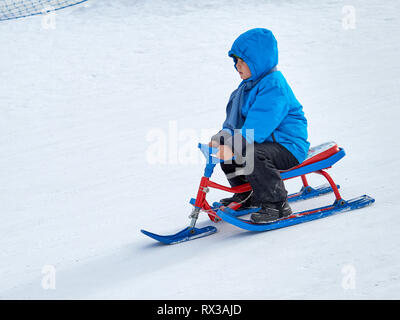 Il ragazzo corse scooter neve dalla montagna di puro bianco della neve in inverno. Foto Stock