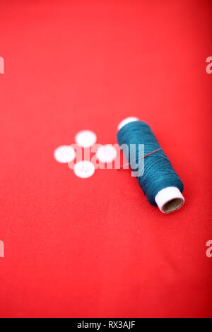 Ritratto di un filo di cucitura con ago e pulsante. Isolato su sfondo rosso. Foto Stock