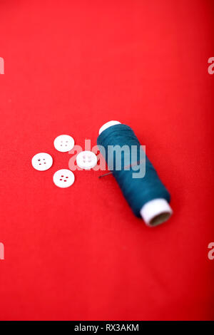 Immagine di un filo di cucitura con ago e pulsante. Isolato su sfondo rosso. Foto Stock