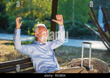 Senior gentleman seduto su una panca in legno e rilassante in un parco Foto Stock