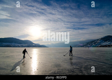 Due persone giocare a hockey su un congelati Lago Okanagan a Kin Beach in Vernon, British Columbia, Canada Foto Stock