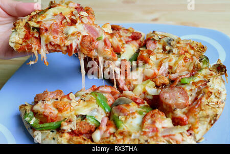 Raccolta a mano un pezzo di succulenti Cheesy Pizza dalla piastra servita su un tavolo di legno Foto Stock