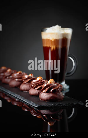 Dolce al cioccolato con granella di nocciole e caffè con panna su un nero sfondo riflettente. Foto Stock